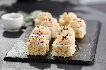 Maki sushi on dark stone table. Sushi roll in seasame and crab topped. Style concept japanesse menu with black background, leaves and hard shadow.