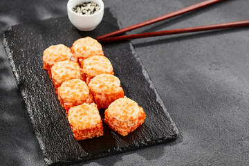 Baked Maki sushi on dark slate. Hot california maki with tobiko. Sushi roll with masago caviar, cheese topped baked oven. Style concept japanese menu with black background, leaves and hard shadow.