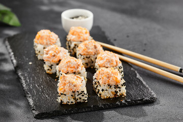 Baked Maki sushi on dark slate. Hot sushi roll with salmon and cheese. Sushi roll sesame outside, baked salmon and cheese topped. Style concept japanese menu with black background, leaves and shadow.