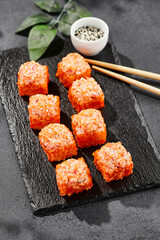 Baked Maki sushi on dark slate. Hot california maki with crab. Sushi roll with masago outside, baked cheese and crab topped. Style concept japanese menu with black background, leaves and hard shadow.