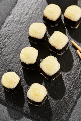 Baked Maki sushi on dark slate. Hot cheese hosomaki roll. Simple sushi roll with cheese, baked cheese topped. Style concept japanese menu with black background, leaves and hard shadow.