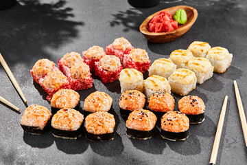 Hot maki set on dark slate. Baked sushi set with variety rolls. Sushi rolls with salmon,tobiko, crab and baked cheese topped. Style concept sushi menu with black background, leaves and hard shadow.