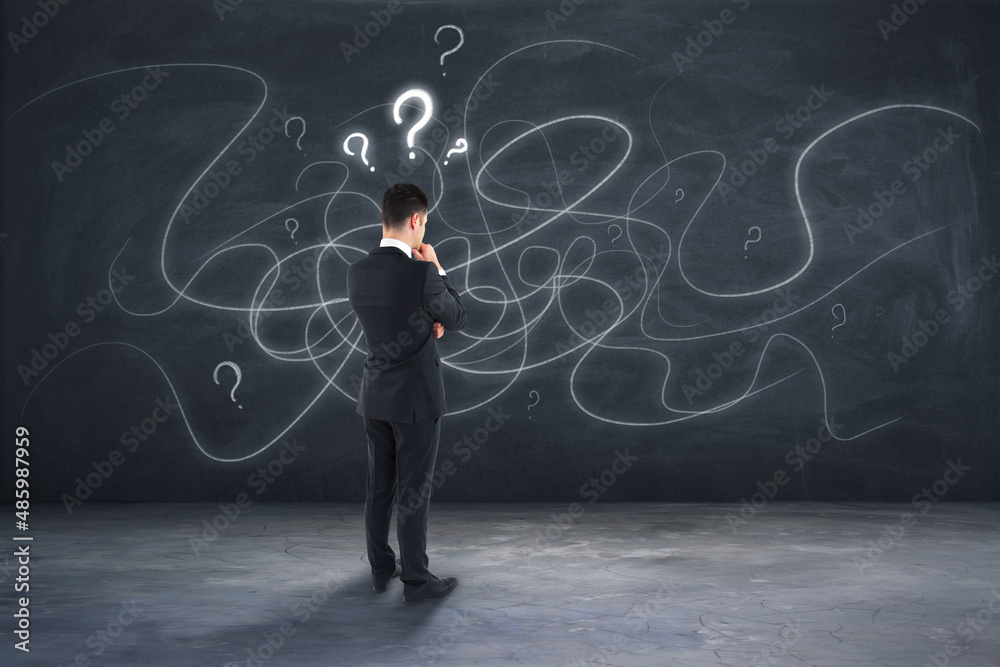 Poster attractive young european businessman standing on concrete background with question marks and scribb