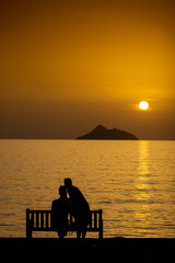 Fototapeta na wymiar Couple relaxing on bench by sea during sunset