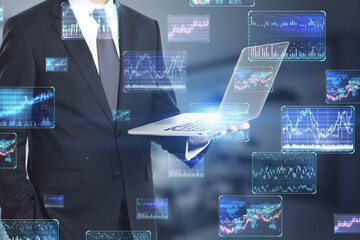 Headless businessman holding laptop with various forex screens on blurry office background....