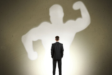Back view of businessman with strong muscle shadow standing on gray wall background. Confidence and...