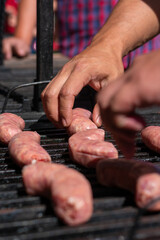 manos acomodando salchichas en el asador , para cocinarlas al carbón en un día soleado  