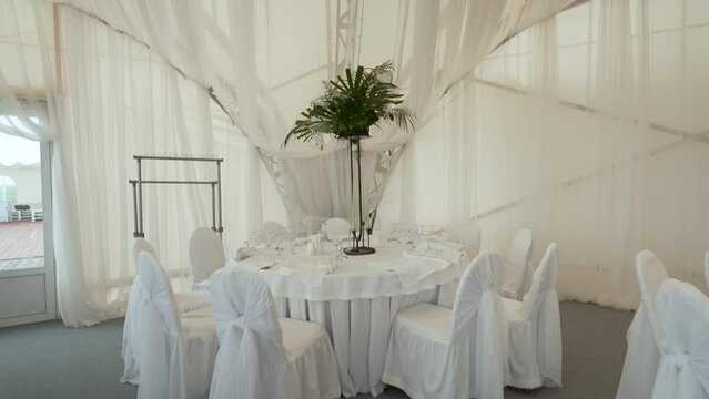 A large banquet hall on the ocean with large empty tables covered with white tablecloths