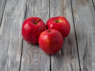 Three red apples on wooden background.