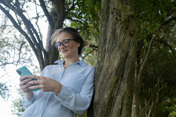 Young woman using a smartphone at day time with a green park in the background. High quality photo