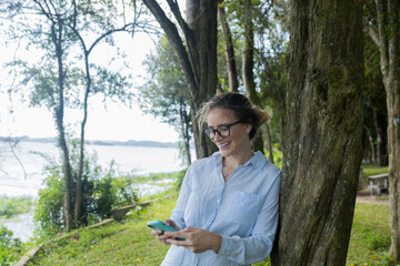 Young woman using a smartphone at day time with a green park in the background. High quality photo