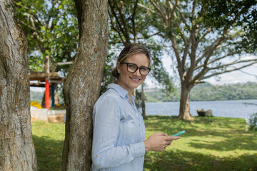 Fototapeta premium Young woman using a smartphone at day time with a green park in the background. High quality photo