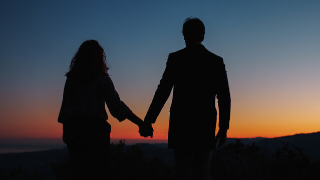 Silhouette of boy and girl holding hands on their backs 