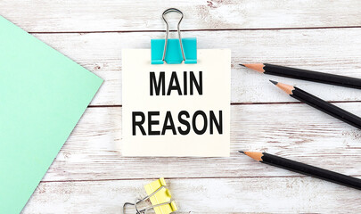 Stickers with pencils and notebook with text MAIN REASON on wooden background