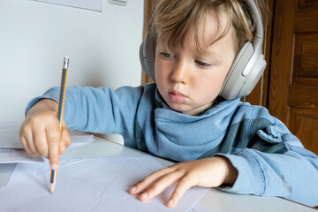 Little boy drawing on paper while listening on headphones