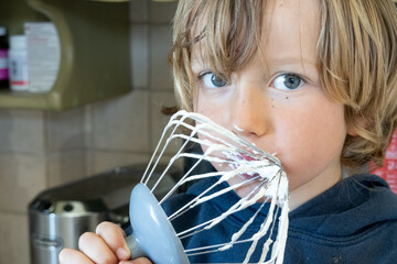 Portrait of little boy tasting whipped cream of wire whisk
