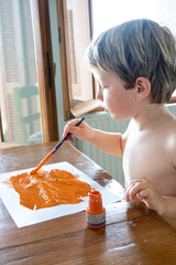 Little boy painting on paper using paintbrush