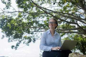 Young woman using a laptop at day time with a green park in the background. High quality photo