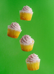 Cupcakes with pink cream in frozen flight on a light green background. Bright festive composition, advertising, banner. Confectionery, supermarket, cafe, restaurant. There is a place to insert.
