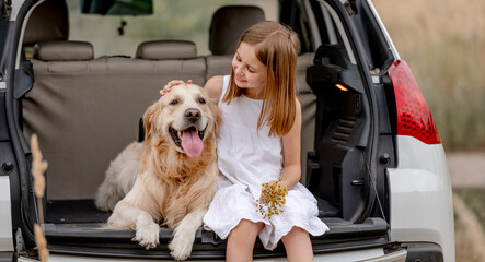 Preteen girl with golden retriever dog in car trunk