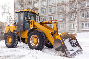 Obraz na płótnie Canvas Big orange tractor cleans up snow from the road and loads it into the truck. Cleaning and cleaning of roads in the city from snow in winter. Snow removal after snowfall and blizzards. 
