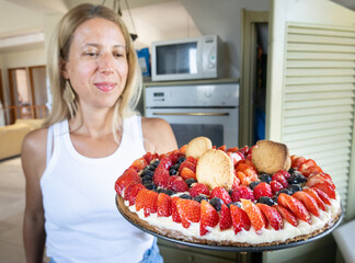 Beautiful woman holding tart garnished with whipped cream, fresh berries and cookies