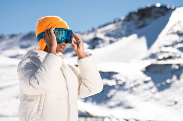 Fototapeta na wymiar A African American woman wearing goggles standing in snowy mountain during winter 