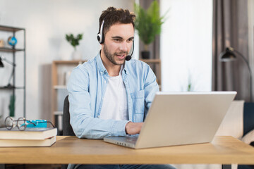 Young caucasian man in headset sitting at desk and having video call on modern laptop. Concept of...