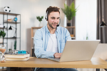 Young caucasian man in headset sitting at desk and having video call on modern laptop. Concept of gadgets, remote work and communication.