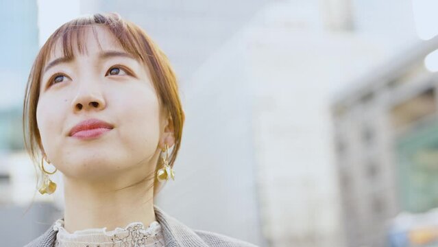 ビル街で空を見上げる若い女性