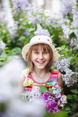 Fototapeta premium European laughing girl in a beige hat and striped dress with a bow in a lilac garden with a basket of lilacs 