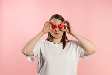 Enjoying young girl with brown hair in a white t-shirt on a pink background and red hearts. High quality photo