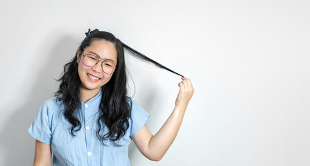Naklejka premium A young asian girl touch her hair smoothly with a big smile on her face. She is wearing a light blue shirt and glasses.
