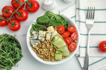 Delicious lentil bowl with blue cheese, tomatoes and cucumber on white marble table, flat lay
