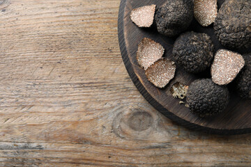 Whole and cut black truffles with board on wooden table, top view. Space for text