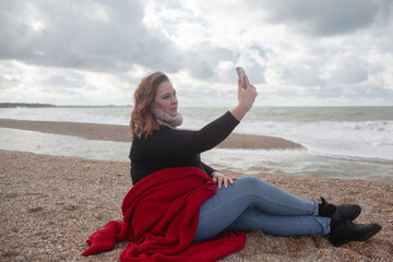 Fototapeta na wymiar Beatuful woman with over weight body walking in the beach, The plus size model wearing jeans, the warm knitted blanket and sweater. the wind in the bich have fun with hairs