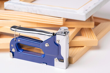 A stapler gun for canvas stretching, wooden frames and a finished canvas in the background. The...