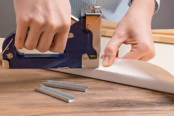 Stretching the canvas on a stretcher in the artist's studio. Women's hands with a stapler fasten...