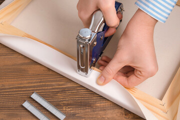 The artist stretches the canvas on a wooden frame with a stapler, top view