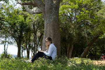 Young woman using a laptop at day time with a green park in the background. High quality photo