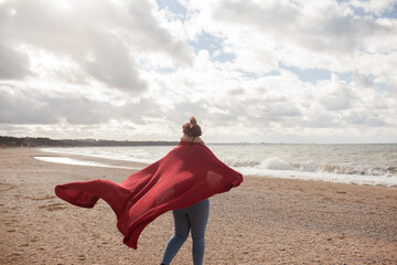 Back view of woman with over weight body walking in the beach, The plus size model wearing jeans, the warm knitted blanket and sweater. the wind in the bich have fun with hairs