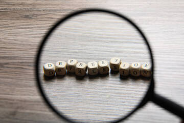 Word Depression made of wooden cubes on table, view through magnifying glass