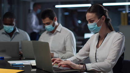 Fototapeta na wymiar Multiethnic businesspeople wearing safety mask work on laptop in open space office