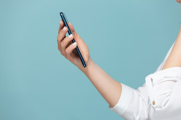Close-up of a woman's hand with a smartphone on which there is a white screen for advertising, on a blue background. Copy paste.