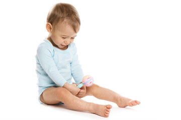 Little boy in romper sitting and playing with plastic rattle.