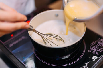 A pastry chef prepares custard on an induction cooker. Stir the resulting cream with a whisk