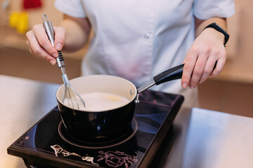 A pastry chef prepares custard on an induction cooker. Stir the resulting cream with a whisk