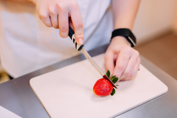 Pastry chef girl slices strawberries with a knife to decorate cakes