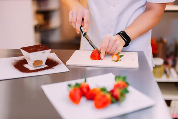 Obraz na płótnie Canvas Pastry chef girl slices strawberries with a knife to decorate cakes. pastry chef cut strawberries for cake and pastries