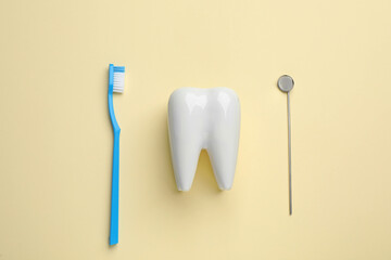 Tooth shaped holder, brush and dentist's mirror on pale yellow background, flat lay